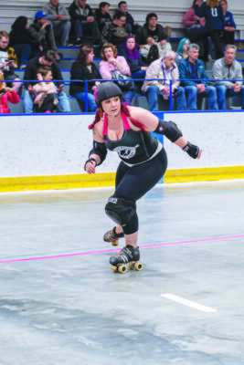 woman on roller skates, wearing knee and elbow pads and helmet, skating on roller derby rink