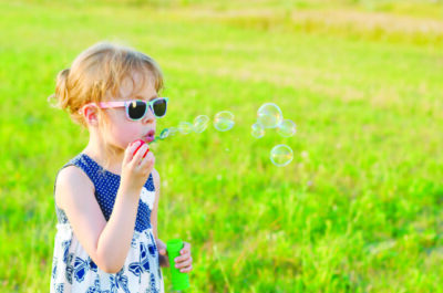 Beautiful girl blowing bubbles in the park, free space. Summer background, happy childhood.