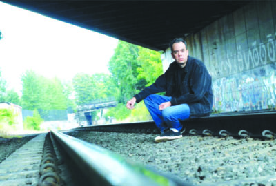 man sitting on railroad tracks under bridge