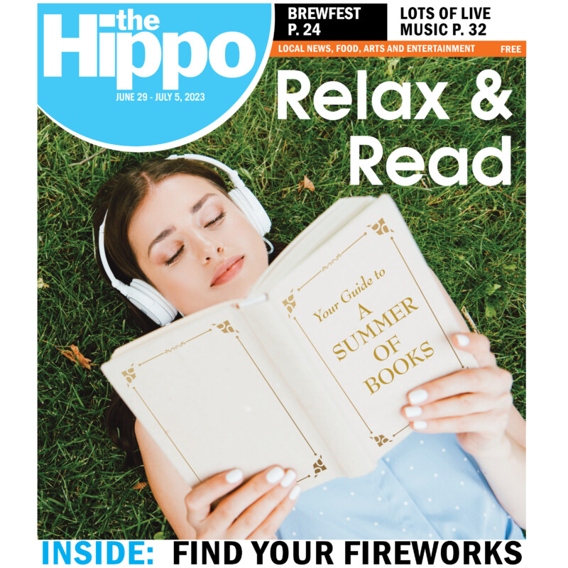 Hippo frontcover with young woman lying in grass, reading book and wearing headphones