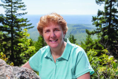 middle aged woman with short hair, posing in front of scenic vista of mountain and trees