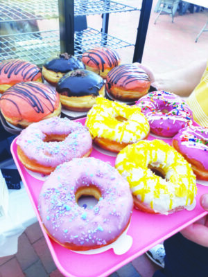 trays of doughnuts in flavor varieties on outdoor table at farmers market