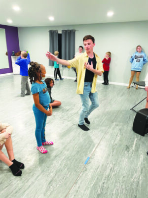 young man in open dance studio, showing younger children how to dance