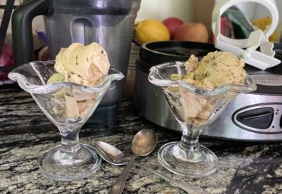 2 fancy cups of ice cream sitting on counter beside blender and spoons