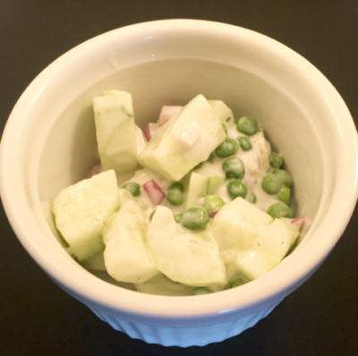 small, round dish containing cut up cucumber with peas, covered in creamy sauce