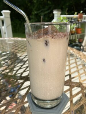 tall glass of iced coffee with straw, sitting on patio table