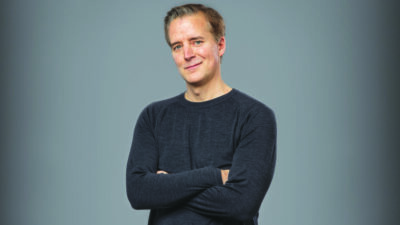 studio photo of man in long sleeve shirt, arms crossed, grinning and looking at camera