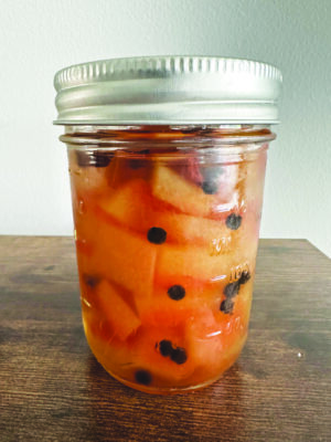 small mason jar filled with pickled watermelon and peppercorns, sitting on table