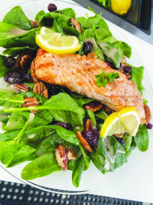fish on leafy salad with pecans and lemon slices, on plate