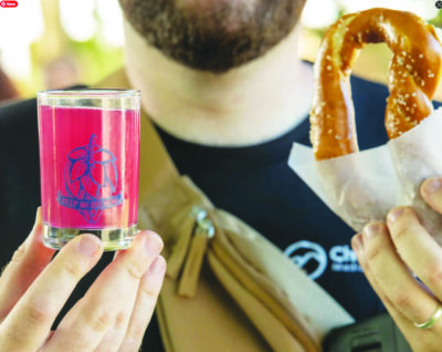 man, head cut off at top of photo, holding shot glass printed with NH Brewers Association logo, and large soft pretzel
