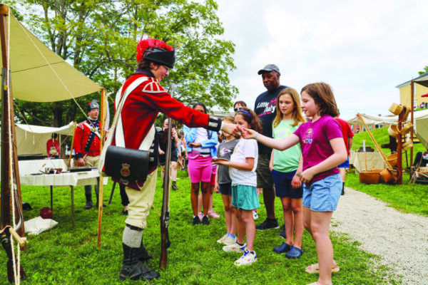young man dressed in historical army costume talking with group of girls during outdoor history event