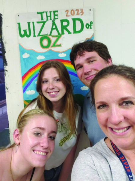 a woman and 3 teenagers putting heads together to take selfie in front of hand made poster for production of The Wizard of Oz
