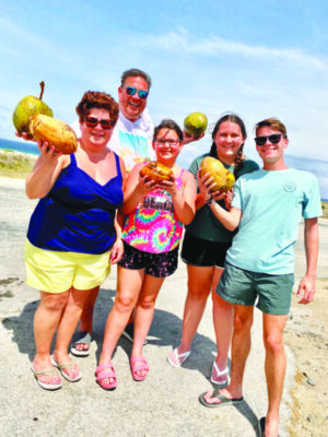woman, man and 3 teenagers holding up exotic fruit and posing on a beach