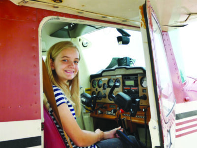 young girl sitting in small, plane in front of controls