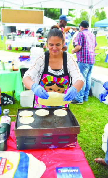 woman placing round, flat tortillas on grill at outdoor event