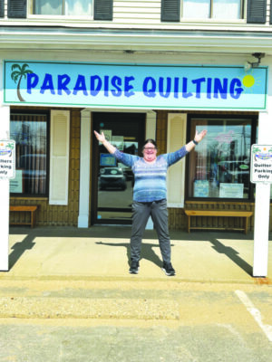 woman wearing sweater standing outside storefront with banner hanging, her arms raised in victory