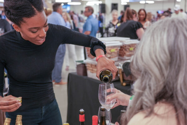 woman pouring wine into visitor's wineglass at indoor event