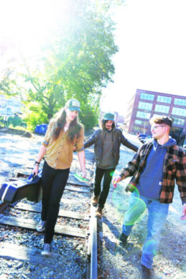 3 band members carrying instruments while walking over train tracks in promotional photo