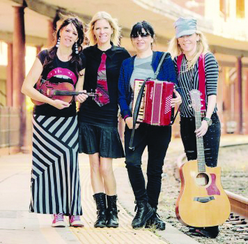 4 female band members standing on small street, one holding guitar, one holding accordian