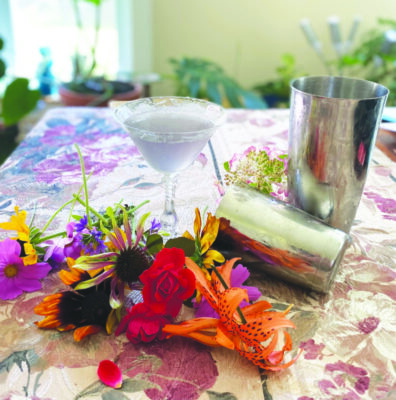 cocktail in martini glass on table with decorative flowers and cocktail shaker