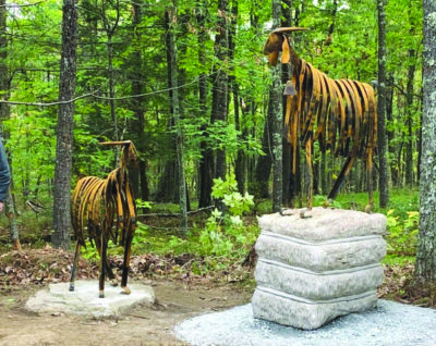 Two sculptures of mountain goats, made with welded and bent metal. Mounted on stacked stone.