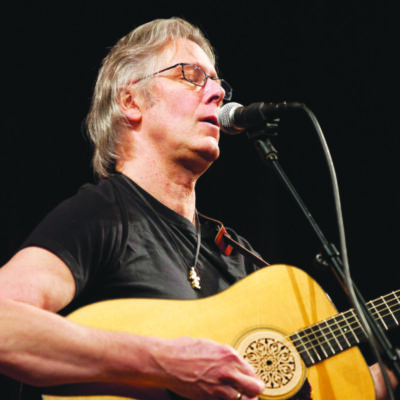 Image of musician Jon Pousette-Dart on stage playing the acoustic guitar.