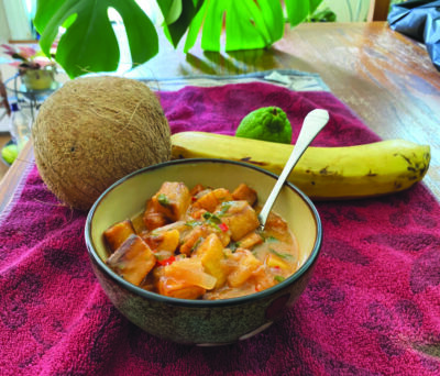 bowl of stew with large chunks of plantains, beside ingredients coconut, plantain and lime