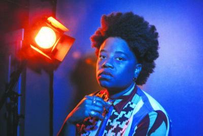 studio portrait of black woman with afro, looking serious at camera under theatrical lights