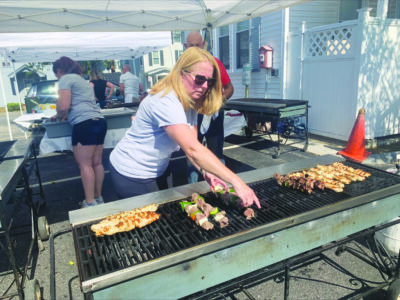 woman under outdoor event tent cooking meats on large grill