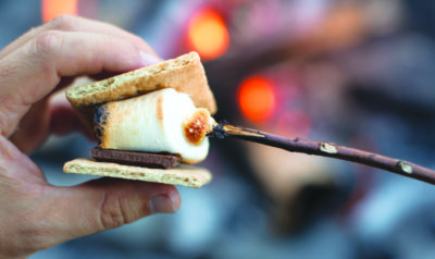 Closeup of person roasting marshmallow enjoying s'more by a camp