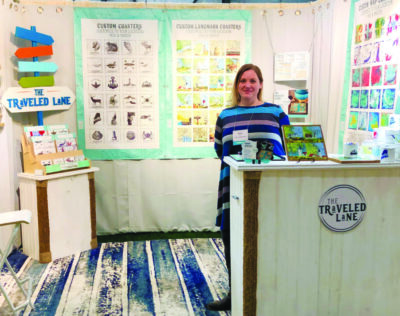 woman in trade booth at craft show, displaying decorative tiles and coasters