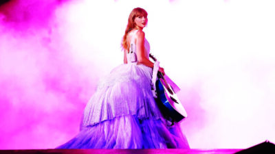 Taylor Swift in promo photo wearing dress with very puffy skirt, looking backwards over her shoulder, carrying guitar