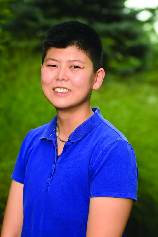 young Asian man standing outside, smiling, posing for headshot