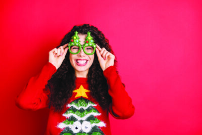 Photo of funny curly lady in playful mood toothy smiling excited to start chilling, wear funky evergreen trees form specs knitted pullover isolated red color background
