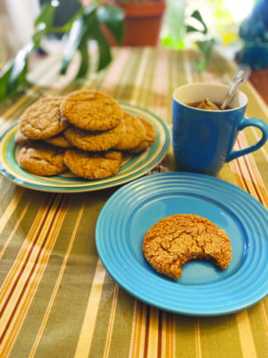 plate of cookies beside mug of tea, second plate with one cookie, bite taken out