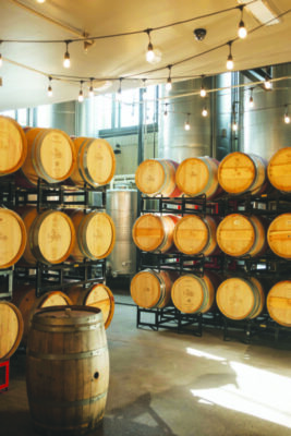 shelves of wine barrels in distillery, decorative string lights hanging from ceiling