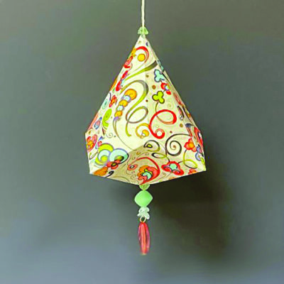 christmas oranment made of colorfully design paper, shaped in a bell, bead and tassel hanging from bottom