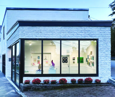 outside of small building with large windows along front and side, artwork hanging on walls and on display stands inside