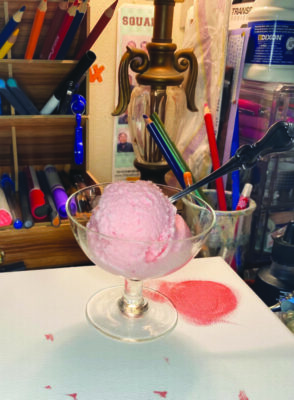 wide bowl shaped glass with stem, on table surrounded by colored pencils and markers, pink ice cream with spoon