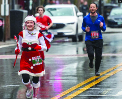 3 runners, one wearing missus santa claus costume running down road on rainy day