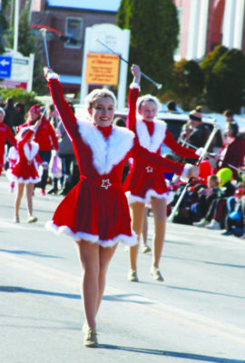 women with batons dressed in red santa dresses walking on sunny day parade