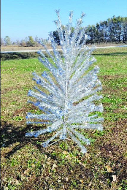 fake silver vintage christmas tree outside on dead grass on sunny day