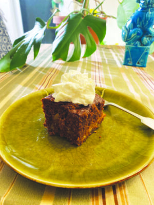 piece of gingerbread cake with dollop of whipped cream on top, on late on table with striped tablecloth