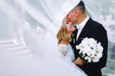 Newlyweds kissing under a flowing veil.