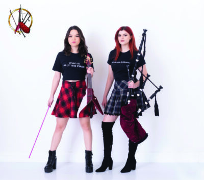 2 young woman wearing plaid skirts, one holding bagpipes and one holding violin and bow, in front of white backdrop