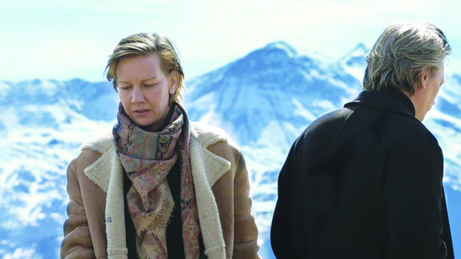 still from Anatomy of a Fall showing a man and a woman facing away from each other, snowy mountains behind them