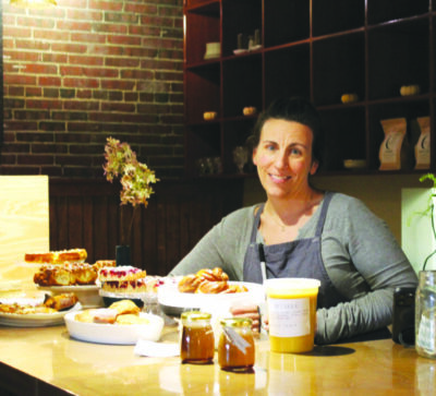 woman sitting behind table filled with baked goods in dark restaurant