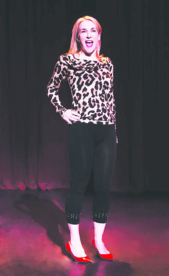 woman wearing black pants and leopard print shirt with red high heels, standing with one hand on hip on stage