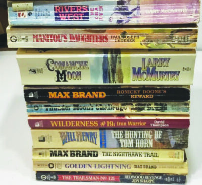 stack of worn paperback books with names and authors printed on the side, books western themed
