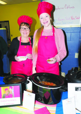 Teenage girl and her grandmother both dressed in a red apron and chefs hat serving chili